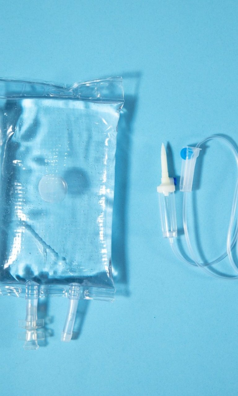 Infusionsbeutel vor blauem Hintergrund und daneben liegt eine Tropfkammer für Infusionen